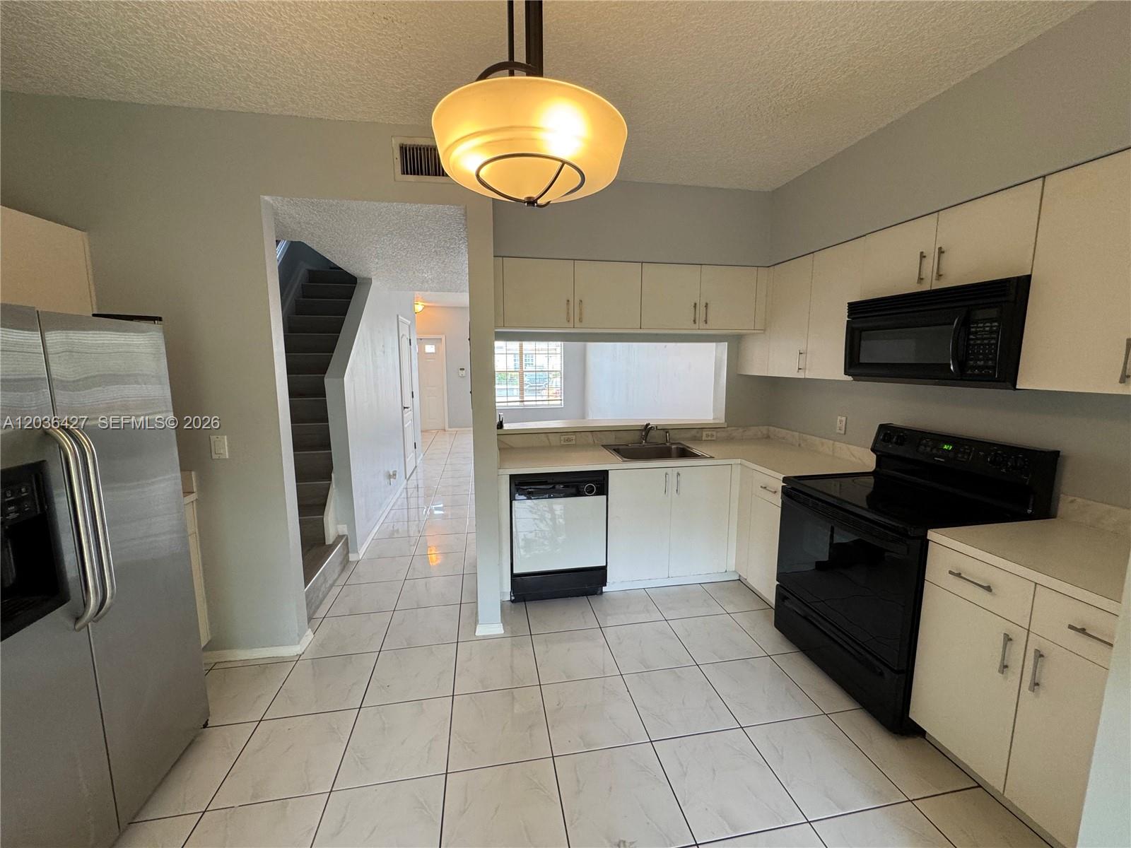 A kitchen with white cabinets, black appliances, and tile flooring leads to a staircase — 77 SIMONTON CR # 77, Weston FL 33326, WESTON, FL