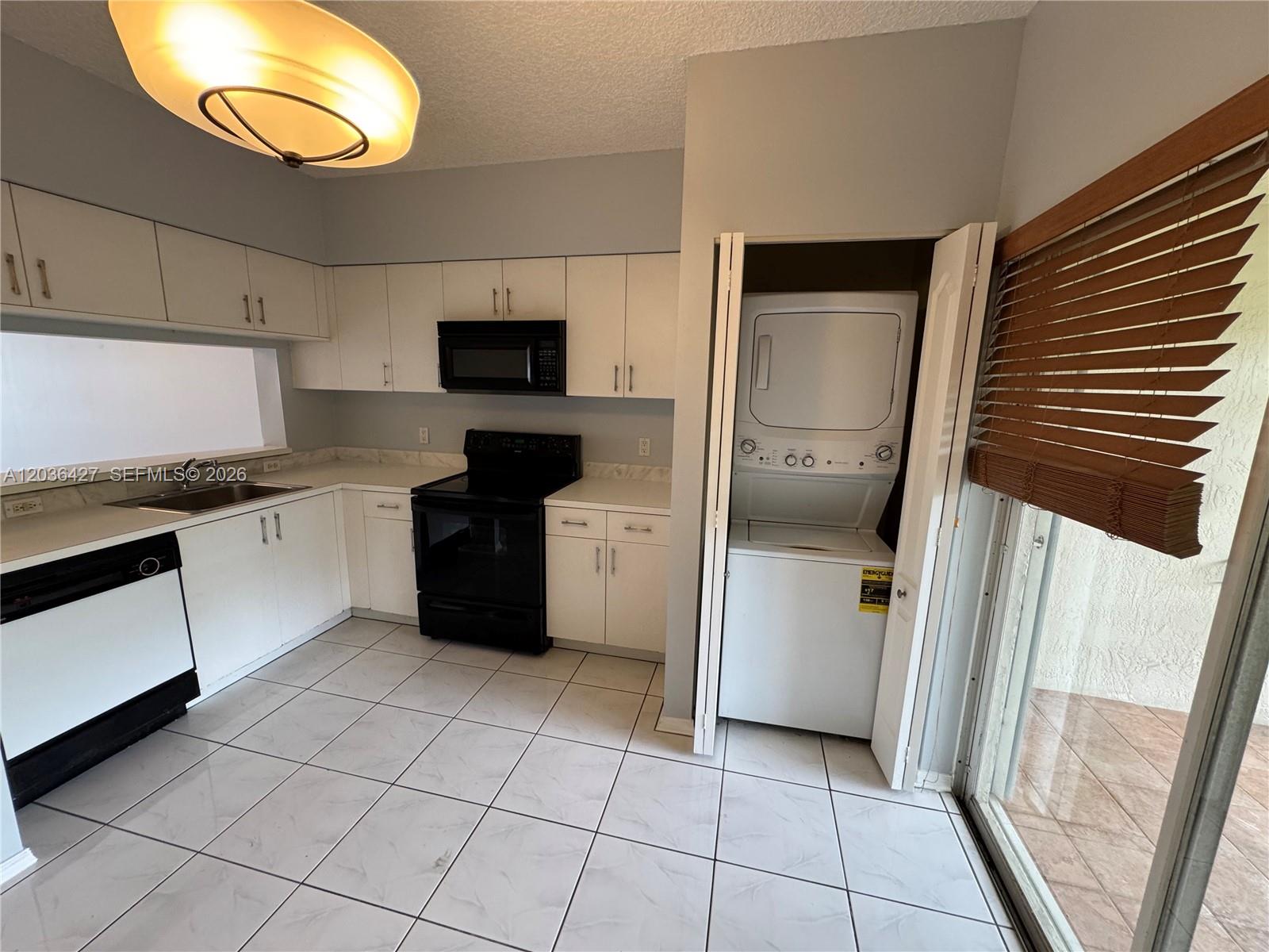 A kitchen features white cabinets, black appliances, tile flooring, and an integrated laundry closet — 77 SIMONTON CR # 77, Weston FL 33326, WESTON, FL