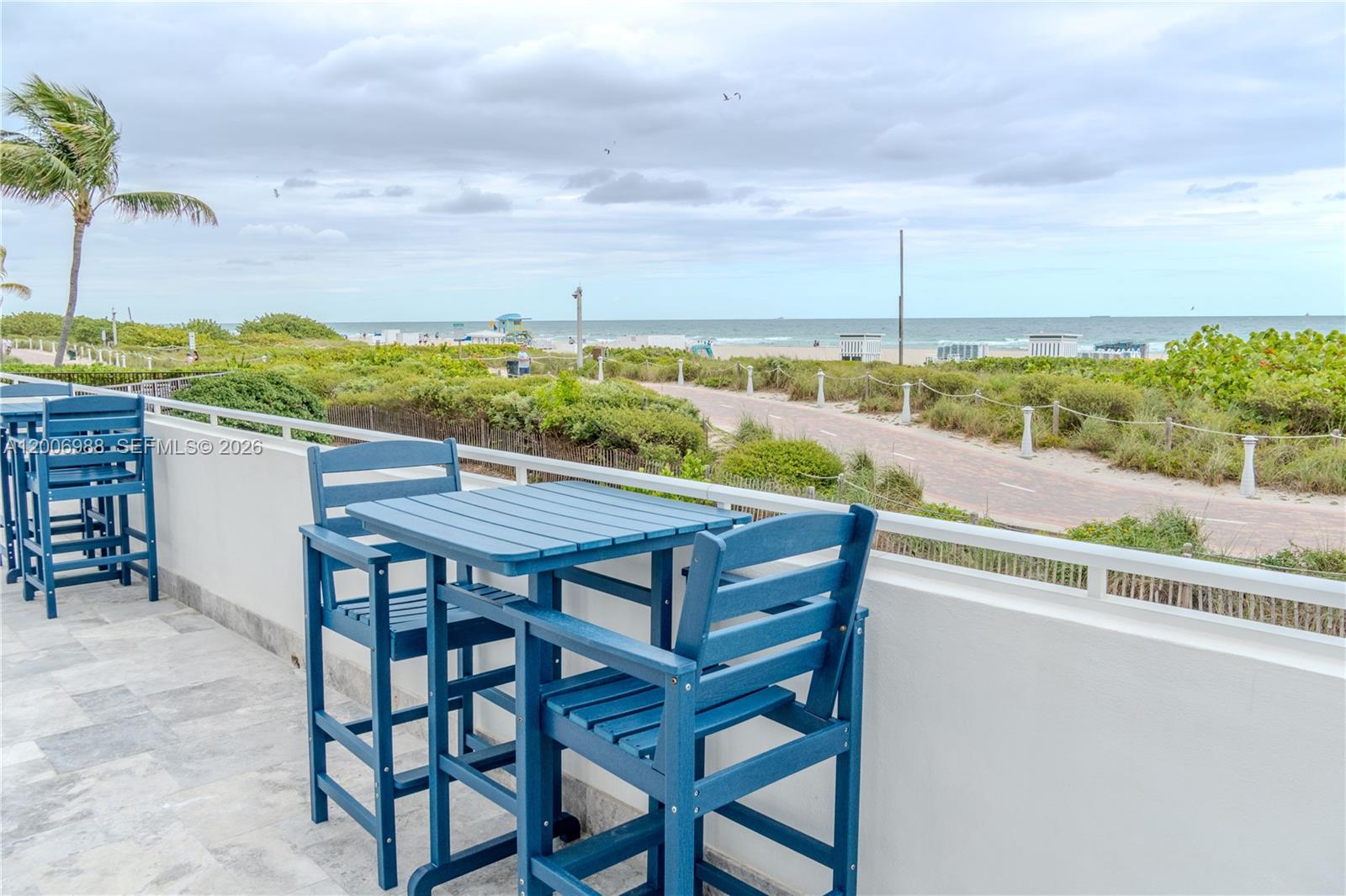 A blue patio table and chairs sit on a balcony overlooking a beach and path — 401 Ocean Dr # 222, Miami Beach FL 33139, MIAMI BEACH, FL