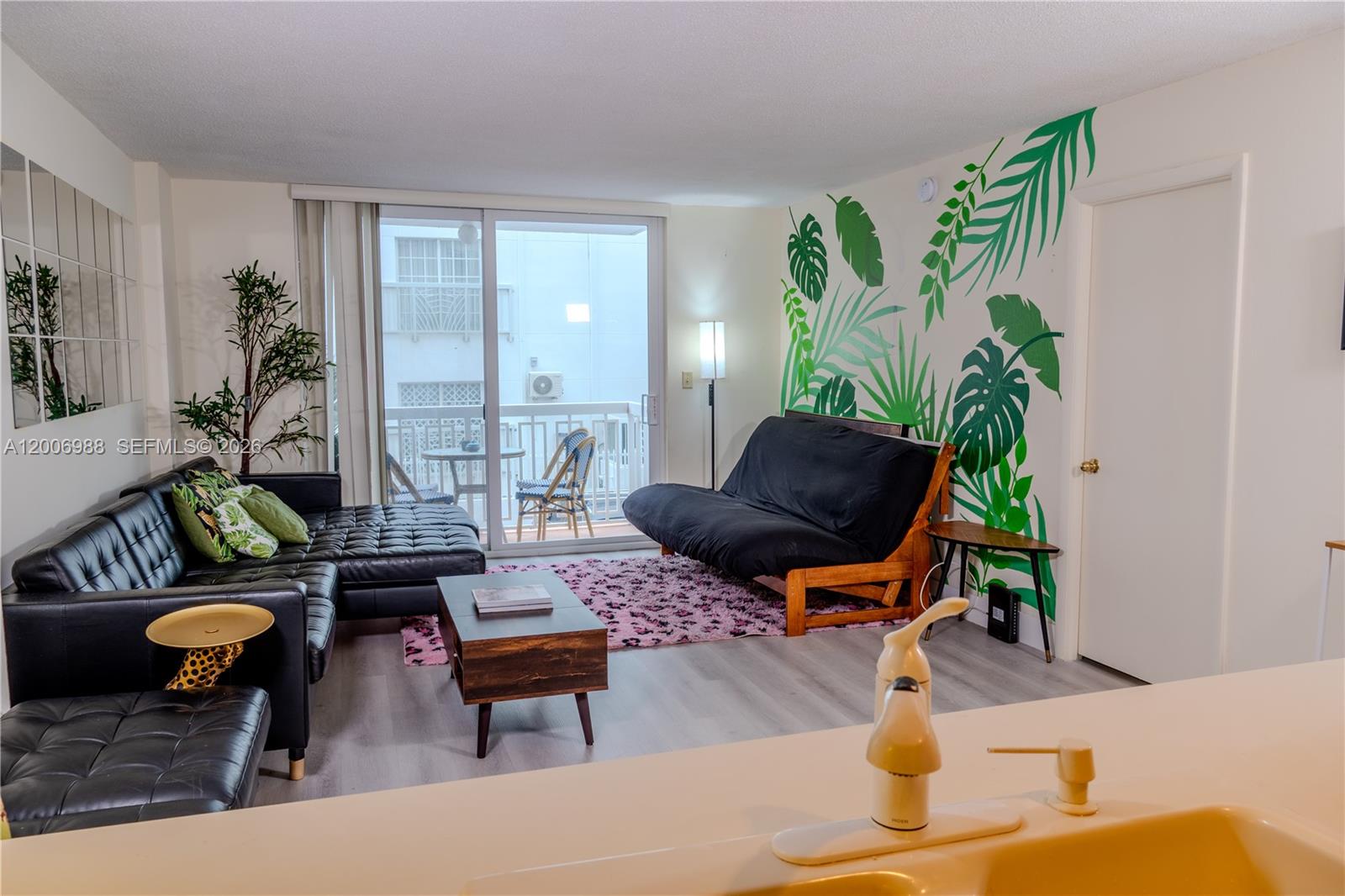 A living room features a black sectional, a futon, and a tropical leaf wall mural — 401 Ocean Dr # 222, Miami Beach FL 33139, MIAMI BEACH, FL