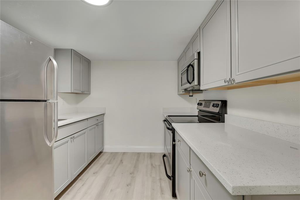 A galley kitchen features gray cabinets, stainless steel appliances, and white speckled countertops — 7225 SEASHORE DRIVE, PORT RICHEY, FL