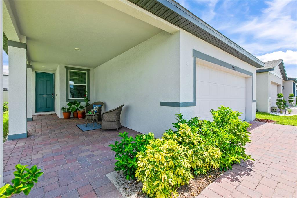 A covered front porch with a brick paver floor, a teal door, and a garage — 3856 GIORGIO DRIVE, WINTER HAVEN, FL