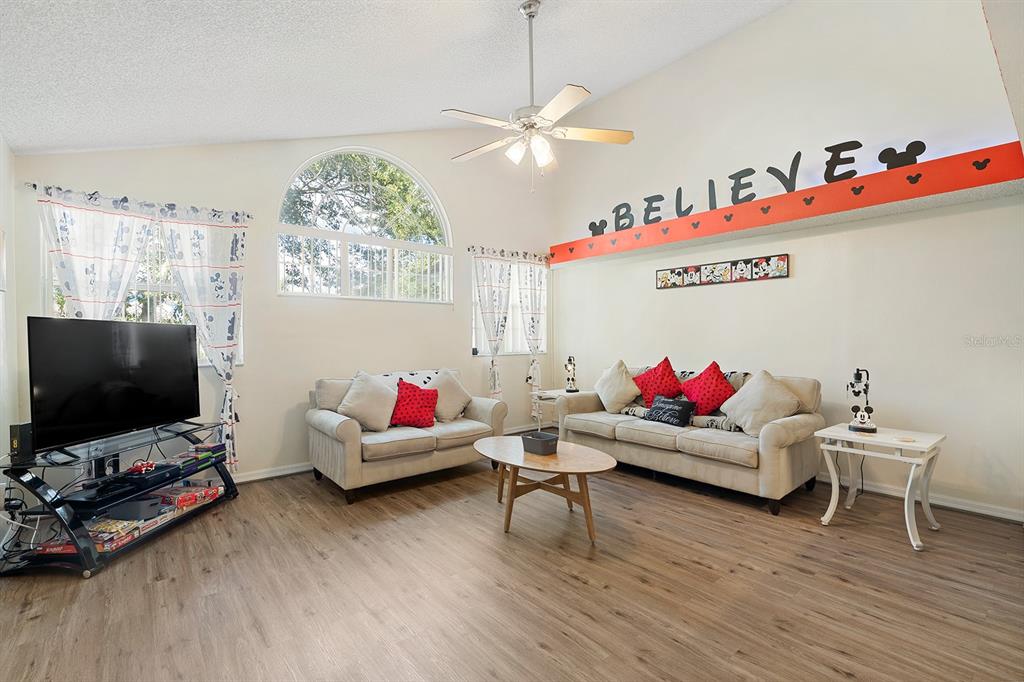A living room features light wood flooring, two sofas, a television, and a vaulted ceiling — 2735 N POINCIANA BOULEVARD UNIT 100, KISSIMMEE, FL