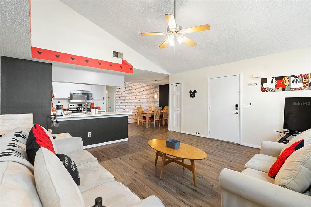 A living room with wood-look flooring, a vaulted ceiling, and Disney-themed decor — 2735 N POINCIANA BOULEVARD UNIT 100, KISSIMMEE, FL