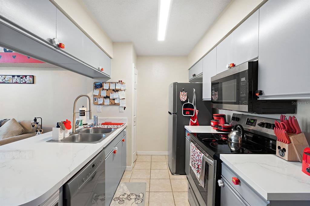 A galley kitchen features gray cabinets, stainless steel appliances, and white countertops — 2735 N POINCIANA BOULEVARD UNIT 100, KISSIMMEE, FL