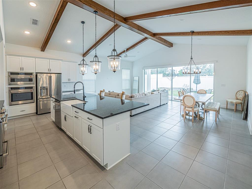A kitchen with white cabinets and a dark island opens into a living and dining area — 13184 DENDY WAY, WINTER GARDEN, FL