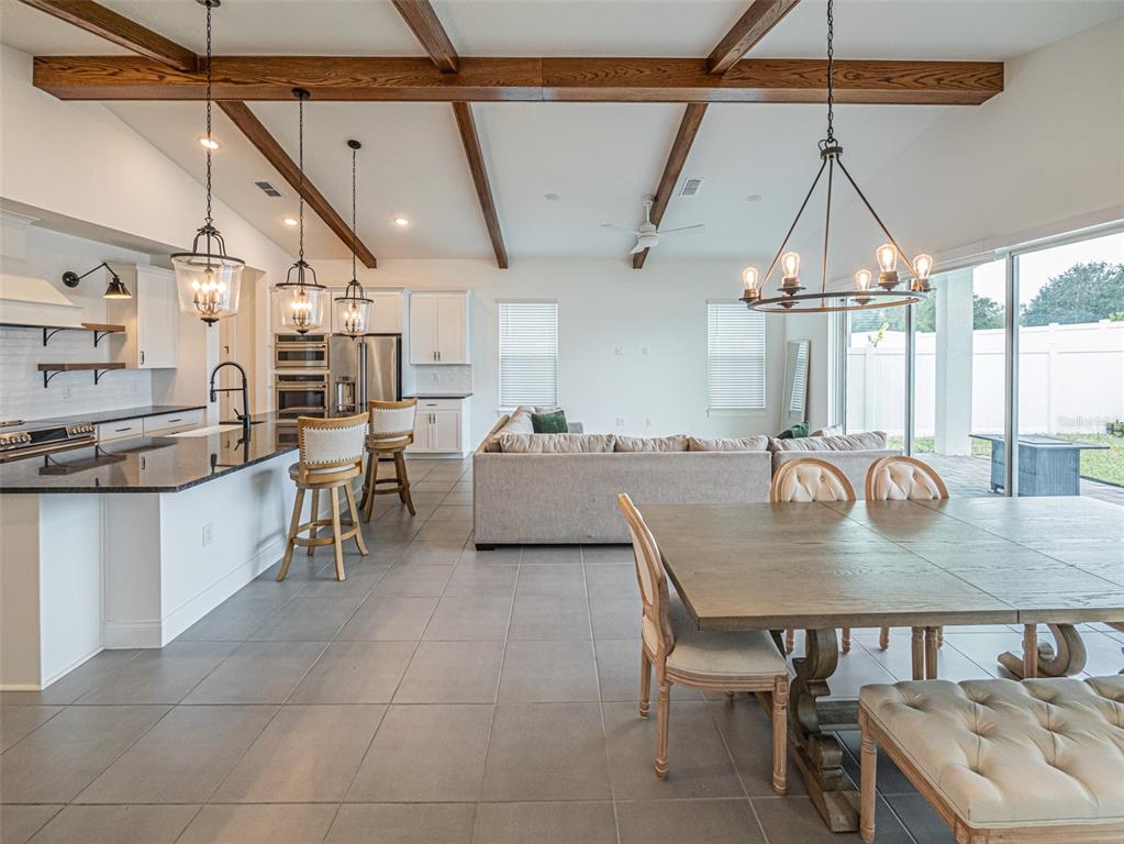An open-concept kitchen, dining area, and living room featuring wood ceiling beams and tile flooring — 13184 DENDY WAY, WINTER GARDEN, FL