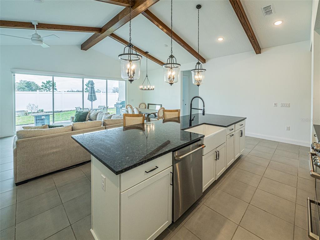 A kitchen island with dark granite countertops sits in an open-concept room with wood beams — 13184 DENDY WAY, WINTER GARDEN, FL