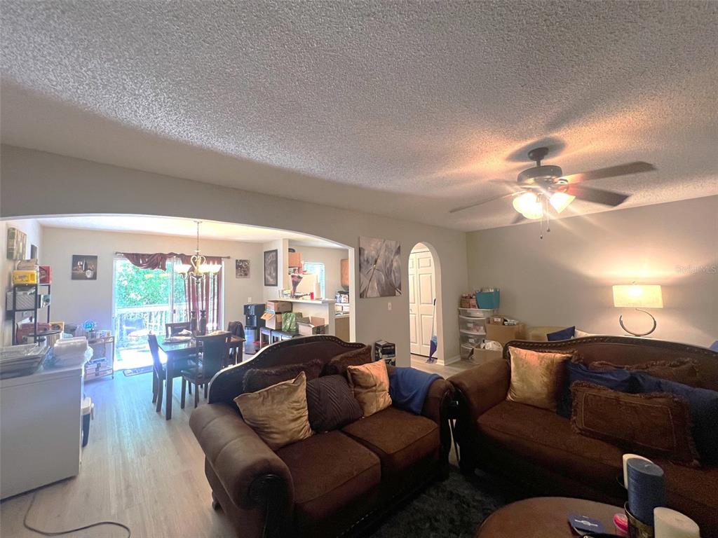 A living room with brown sofas and a dining area visible through an arched opening — 4617 ASHBURN SQUARE DRIVE, TAMPA, FL
