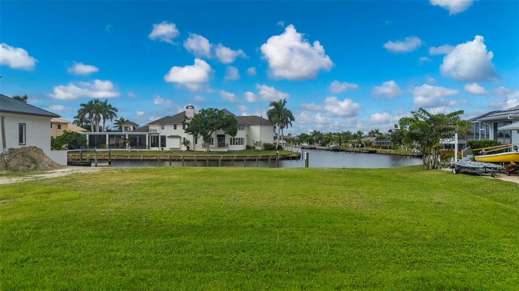 A grassy waterfront lot overlooks a canal with neighboring houses and palm trees under blue skies — 234 BEENEY ROAD SE, PORT CHARLOTTE, FL