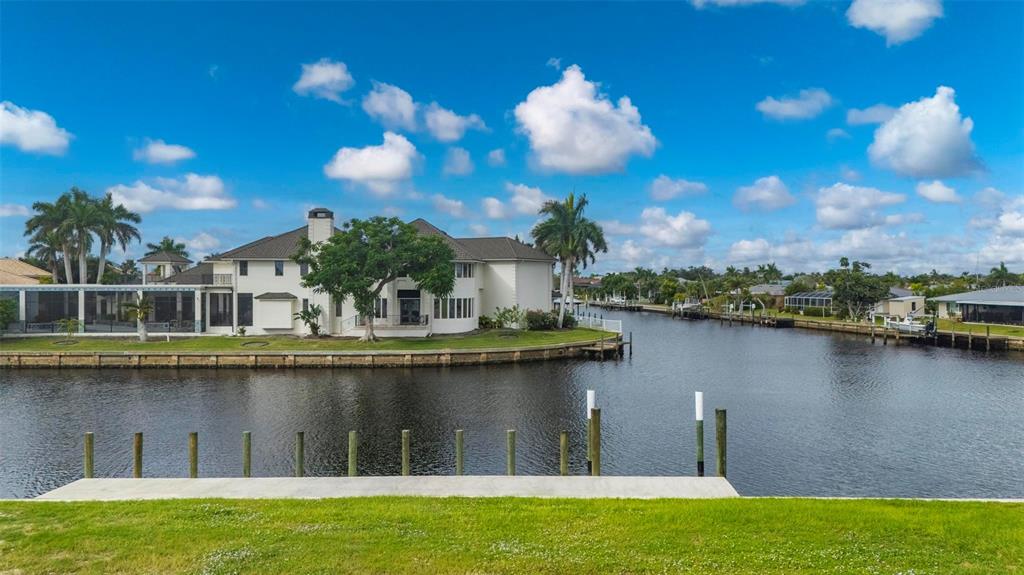 A white house with a large tree sits along a canal with a concrete dock — 234 BEENEY ROAD SE, PORT CHARLOTTE, FL