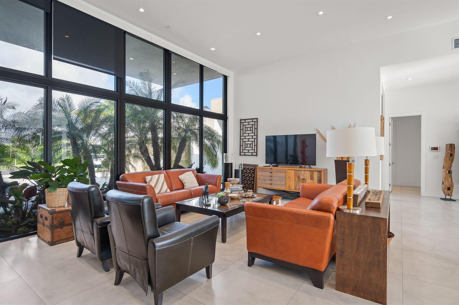 A living room features leather sofas, black armchairs, and floor-to-ceiling windows overlooking palm trees — 16539 N Botaniko Dr Drive N, Weston FL 33326, WESTON, FL