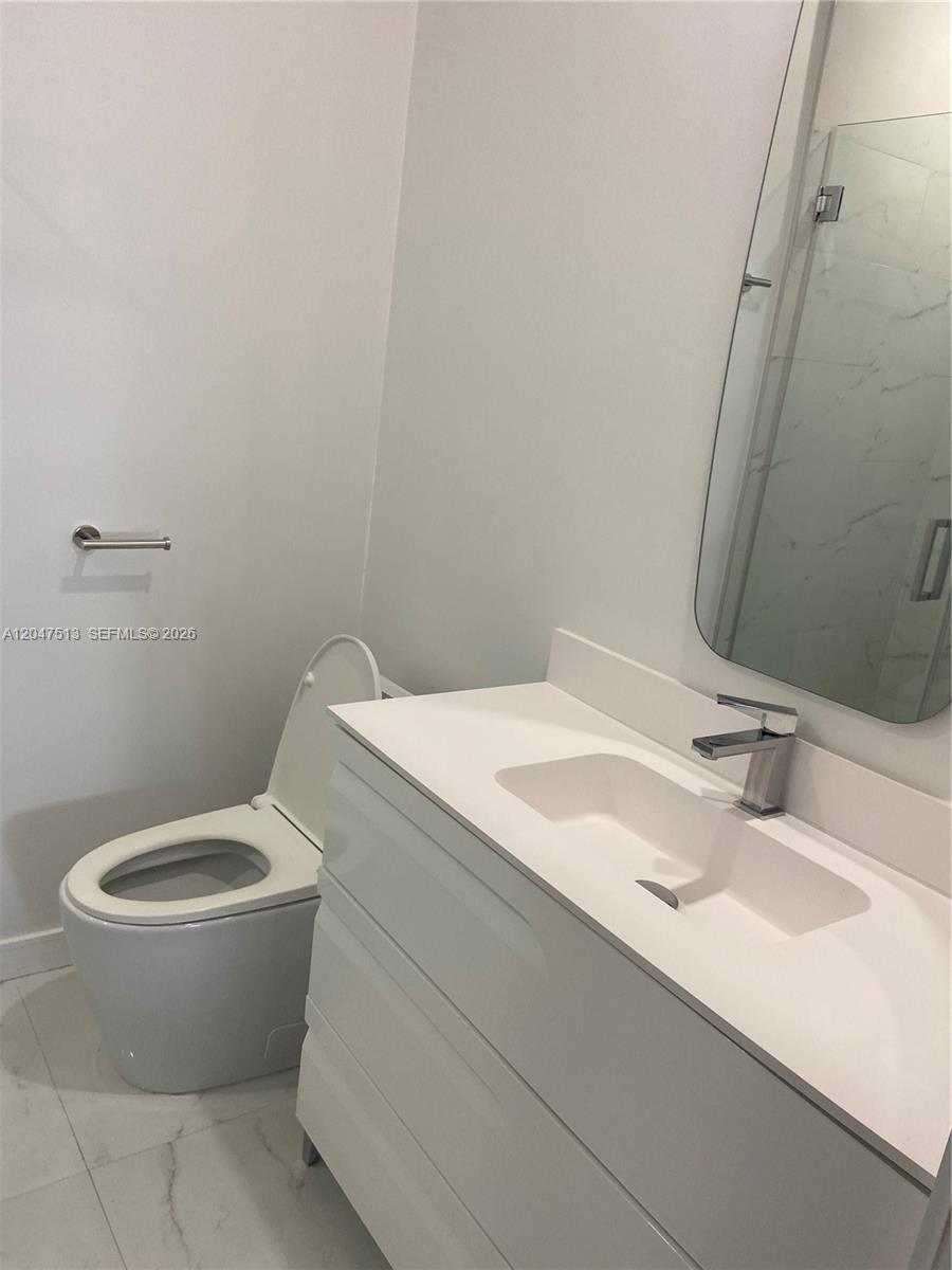 A modern bathroom features a white vanity, a wall-mounted mirror, and a toilet — 1610 Euclid Ave # A105, Miami Beach FL 33139, MIAMI BEACH, FL