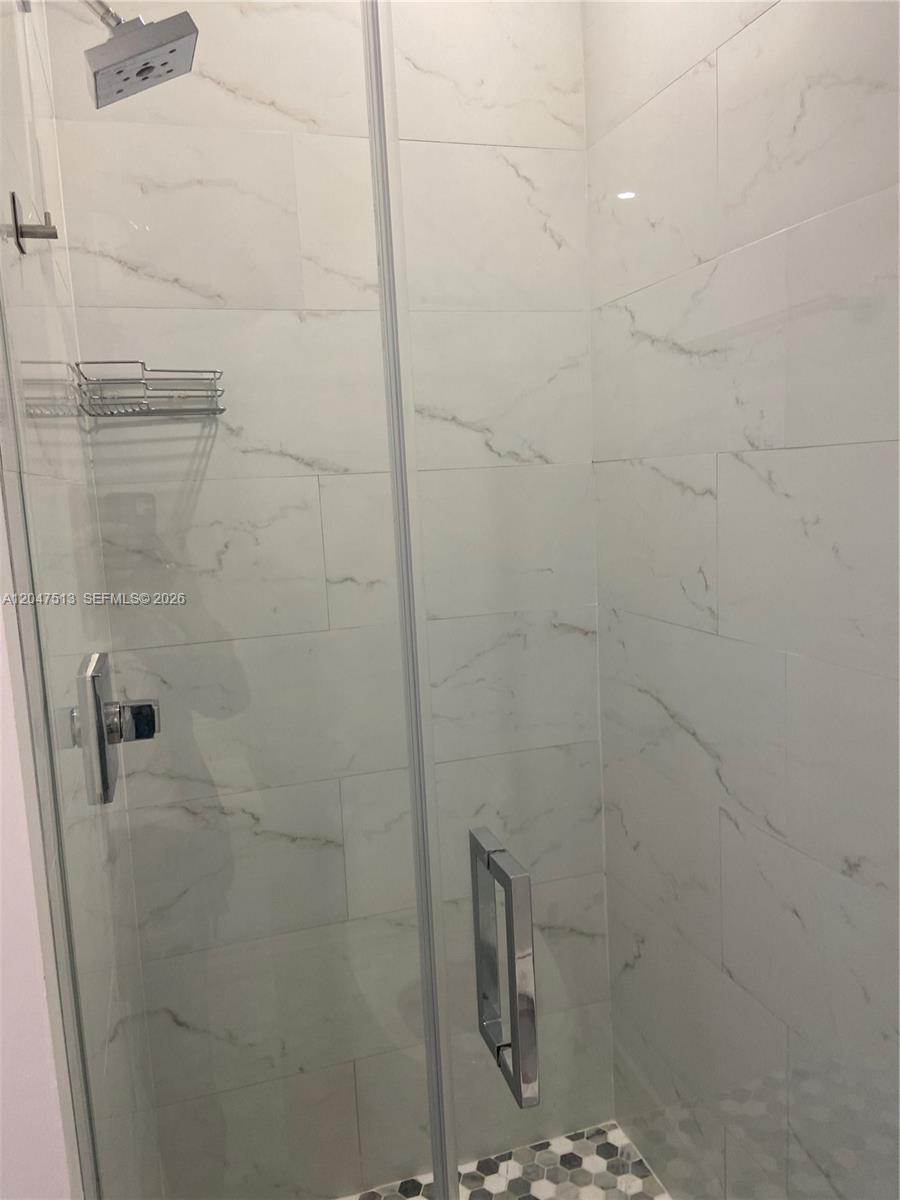 A walk-in shower features white marble-look wall tiles and a hexagonal tile floor — 1610 Euclid Ave # A105, Miami Beach FL 33139, MIAMI BEACH, FL