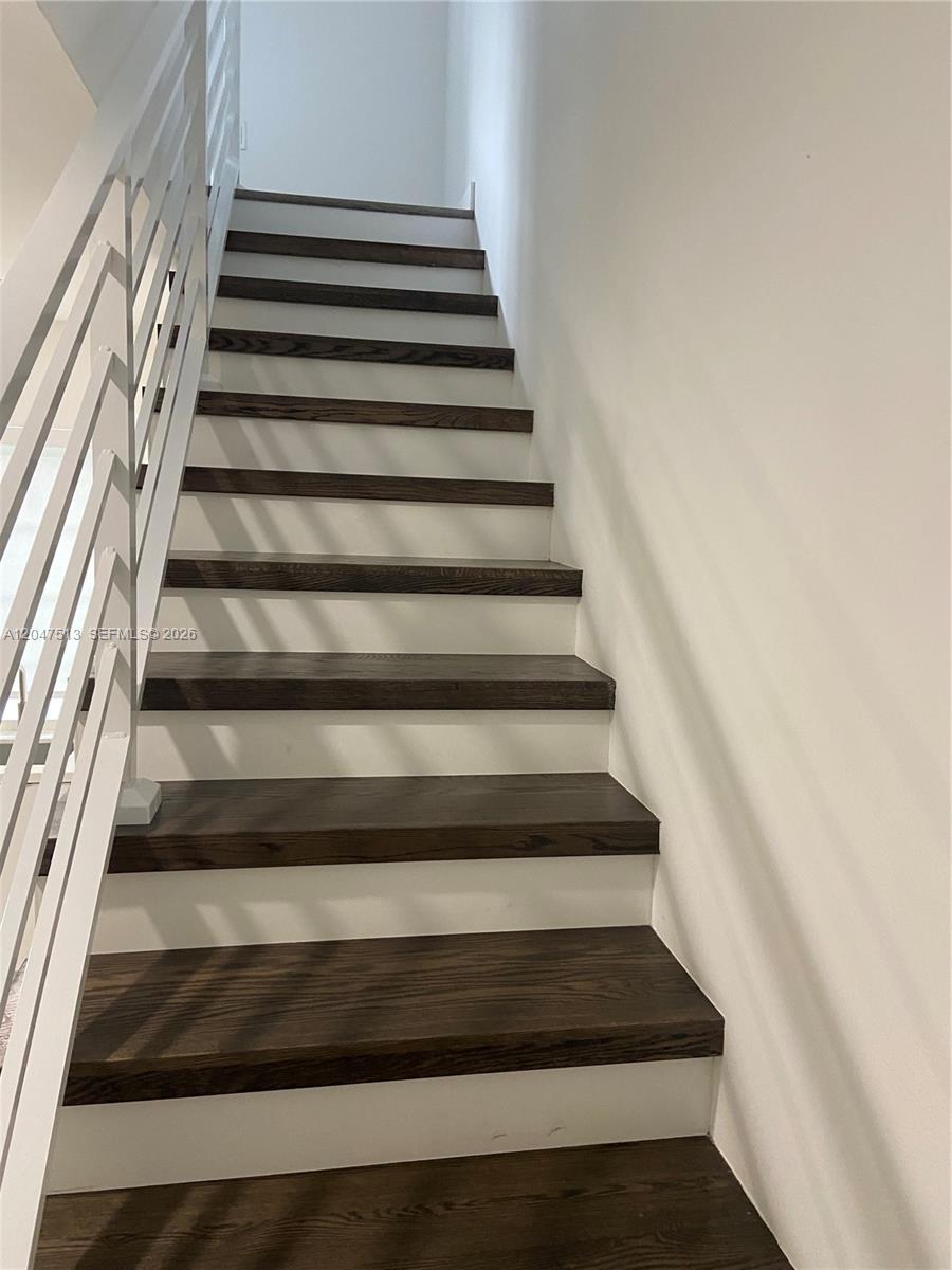 A staircase features dark wood treads, white risers, and a white metal railing — 1610 Euclid Ave # A105, Miami Beach FL 33139, MIAMI BEACH, FL