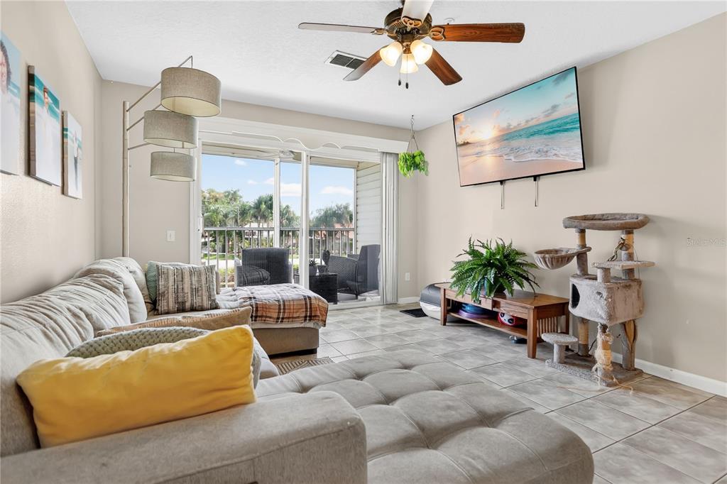 A living room features a sectional sofa, a wall-mounted television, and a sliding glass door — 3930 SOUTHPOINTE DRIVE UNIT 214, ORLANDO, FL