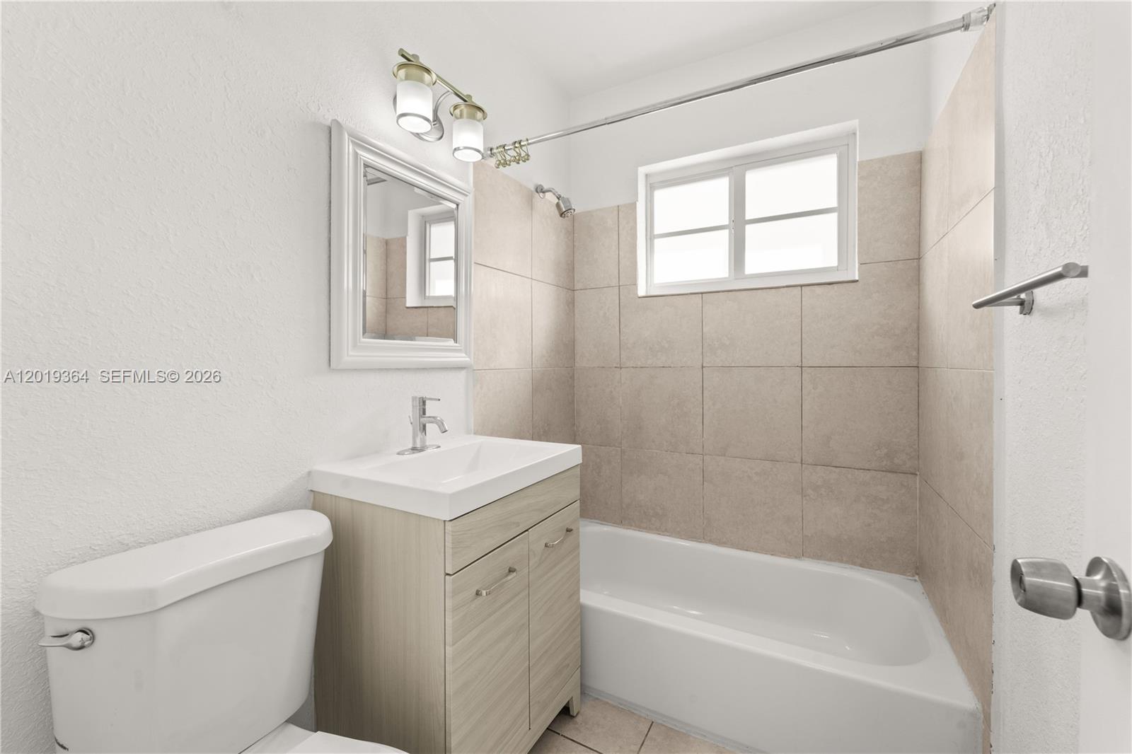 A bathroom features a white toilet, a light wood vanity, and a tiled bathtub shower — 6905 Rue Vendome # 8, Miami Beach FL 33141, MIAMI BEACH, FL