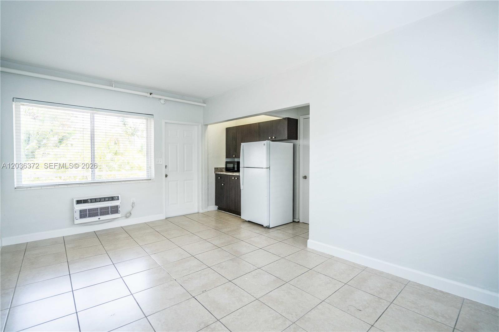 A kitchen with dark cabinets and a white refrigerator sits adjacent to an open area — 8315 Byron Ave # 7A, Miami Beach FL 33141, MIAMI BEACH, FL