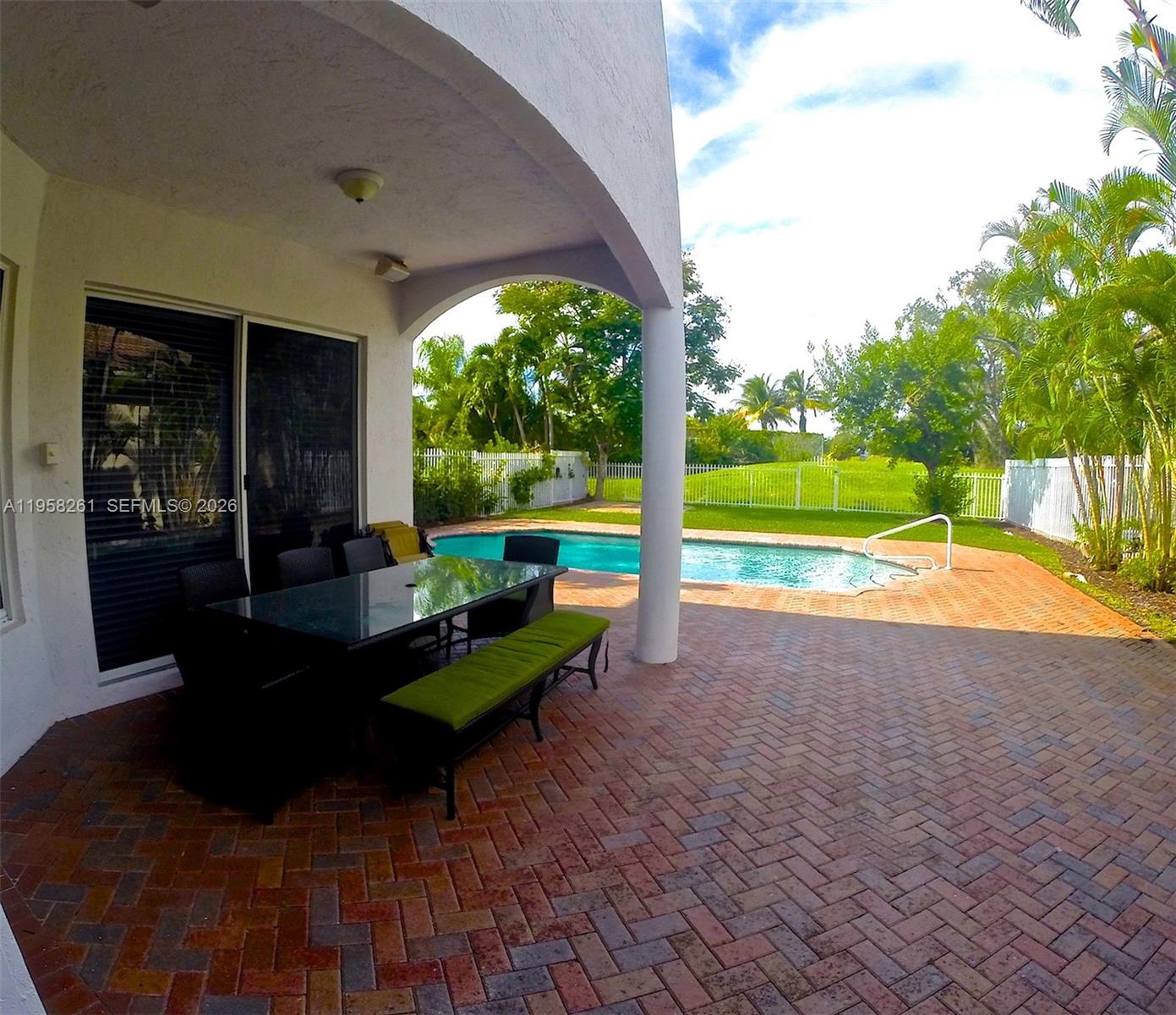 A covered patio with a dining set overlooks a swimming pool and a grassy backyard — 1675 NE 196th St, Miami FL 33179, MIAMI, FL