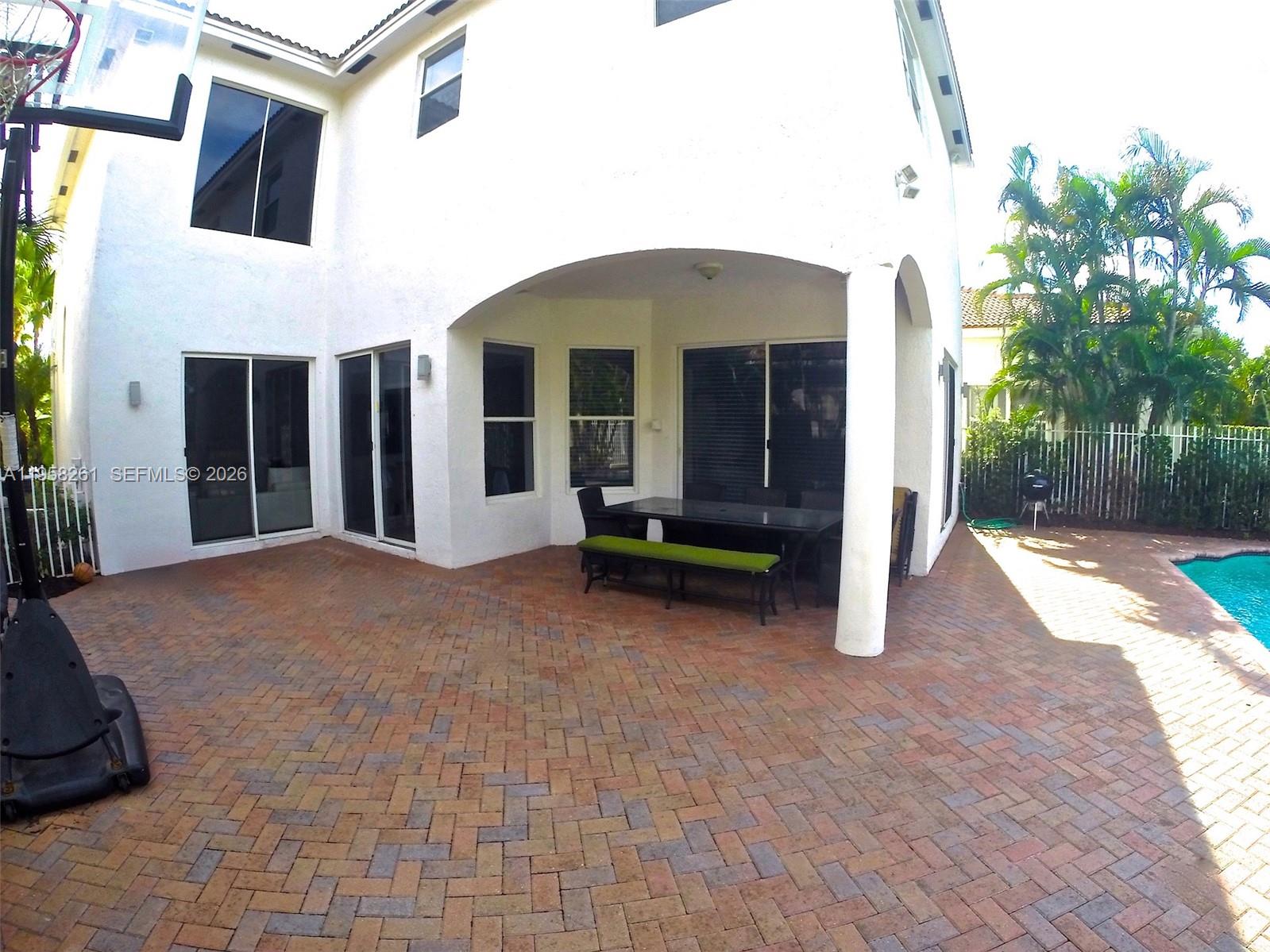 A paved patio features a covered dining area, a basketball hoop, and a swimming pool — 1675 NE 196th St, Miami FL 33179, MIAMI, FL
