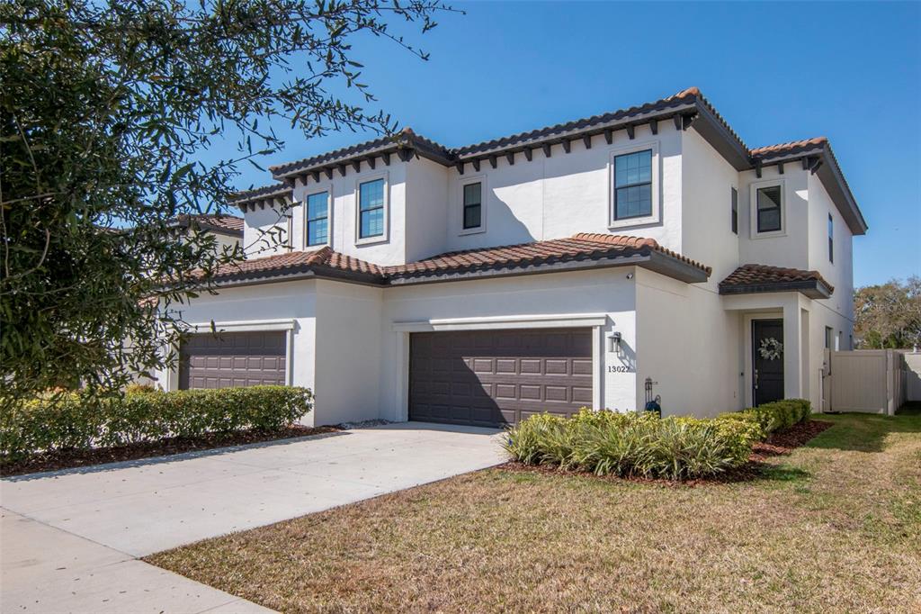 A two-story stucco townhouse with a two-car garage and a tile roof — 13022 SANCTUARY VILLAGE LANE, TAMPA, FL