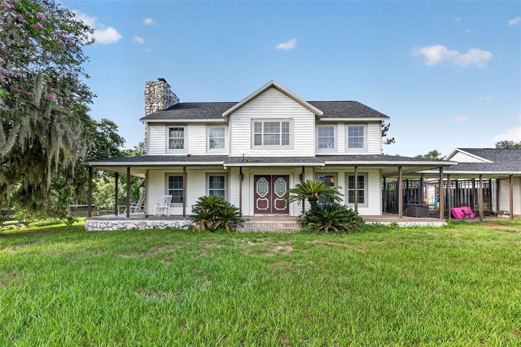A two-story white house with a wrap-around porch and a stone chimney stands outdoors — 8922 PRITCHER ROAD, LITHIA, FL