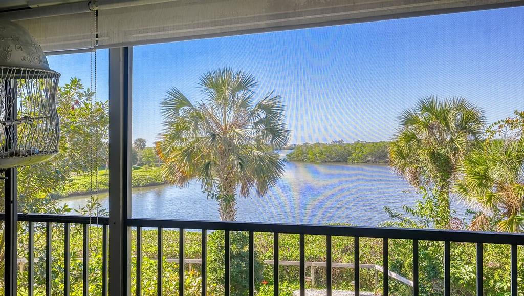 A screened-in balcony overlooks a calm waterway surrounded by lush green trees and palm trees — 1617 BAYHOUSE COURT UNIT BA221, SARASOTA, FL