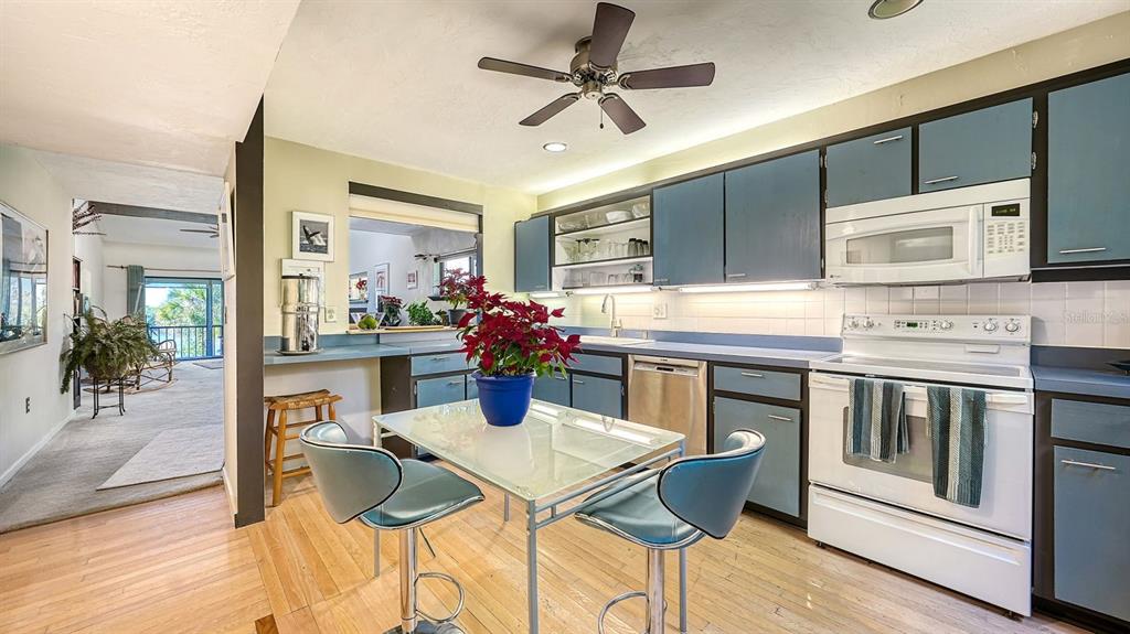 A kitchen features blue cabinets, a glass-topped dining table, and a view into another room — 1617 BAYHOUSE COURT UNIT BA221, SARASOTA, FL