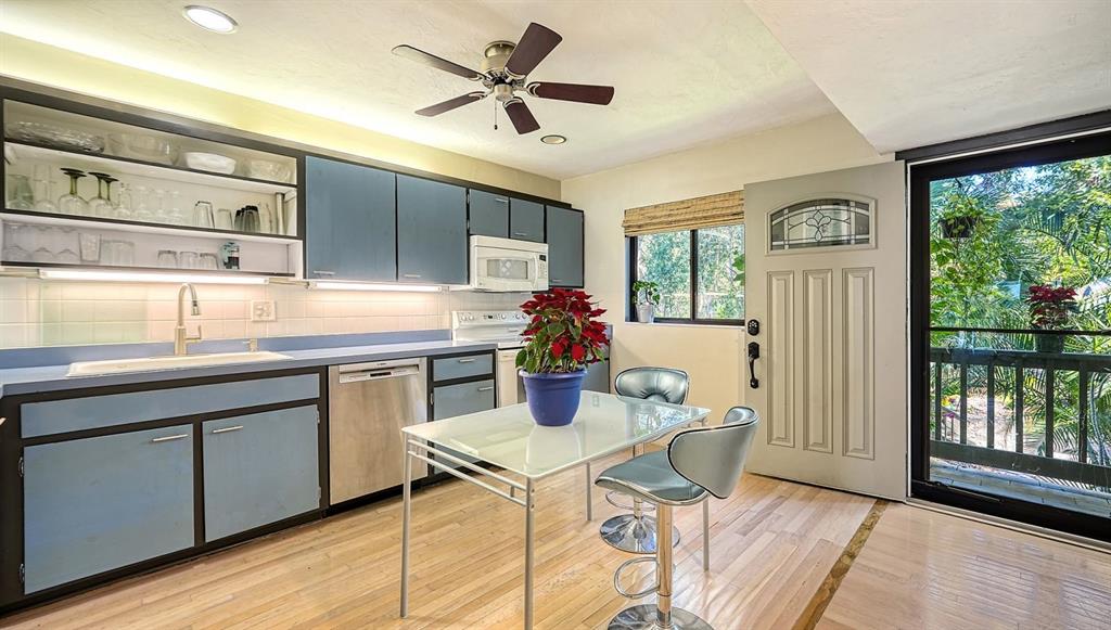 A kitchen features blue cabinets, a glass-top dining table, and a door leading to a balcony — 1617 BAYHOUSE COURT UNIT BA221, SARASOTA, FL