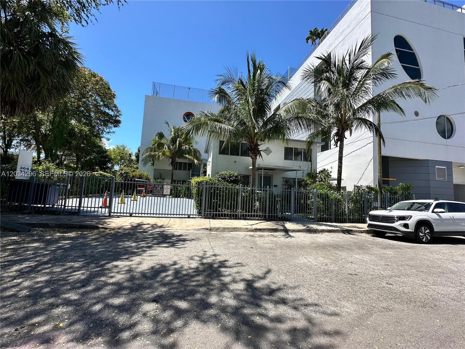A white building with palm trees stands behind a metal fence and a parked car — 364 SW 11th St, Miami FL 33130, MIAMI, FL