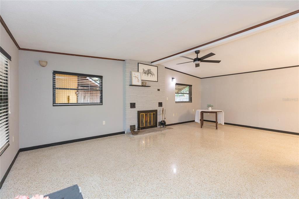 A living room features a painted brick fireplace, terrazzo flooring, and a ceiling fan — 8813 FLAME VINE AVENUE, SEMINOLE, FL