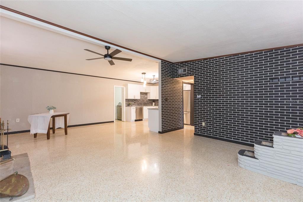 An open-concept living area features terrazzo flooring, a black brick wall, and a kitchen beyond — 8813 FLAME VINE AVENUE, SEMINOLE, FL
