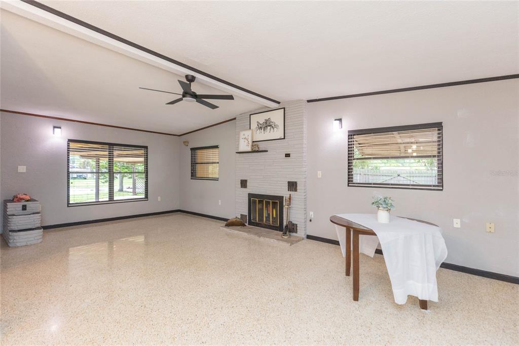A living room features a gray brick fireplace, a ceiling fan, and light-colored terrazzo flooring — 8813 FLAME VINE AVENUE, SEMINOLE, FL