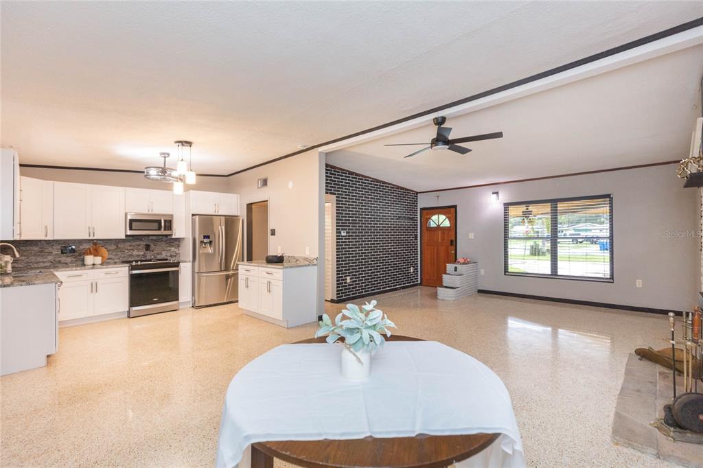 An open-concept kitchen and living area featuring white cabinets, stainless appliances, and terrazzo flooring — 8813 FLAME VINE AVENUE, SEMINOLE, FL