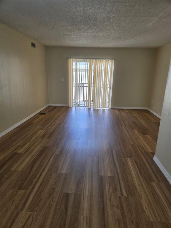 An empty room with wood-look flooring, beige walls, and a sliding glass door with blinds — 1000 LAKE OF THE WOODS BOULEVARD UNIT 201E, CASSELBERRY, FL