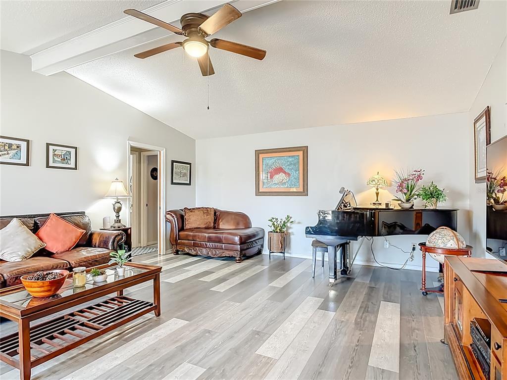 A living room features wood-look flooring, a grand piano, leather furniture, and a ceiling fan — 2091 OLDHAM AVENUE, DELTONA, FL