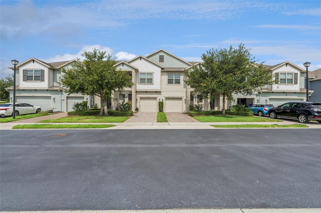 A row of multi-story townhomes with attached garages and paved driveways under a blue sky — 618 MERRY BROOK CIRCLE, SANFORD, FL