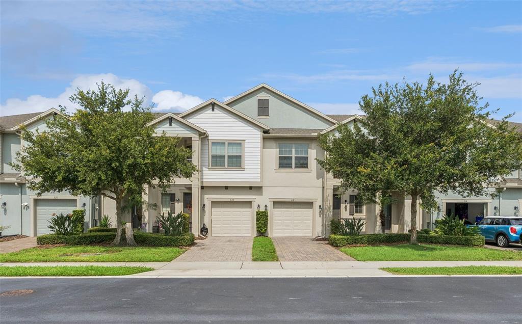A two-story townhouse building with two garages, a paved driveway, and two large trees — 618 MERRY BROOK CIRCLE, SANFORD, FL