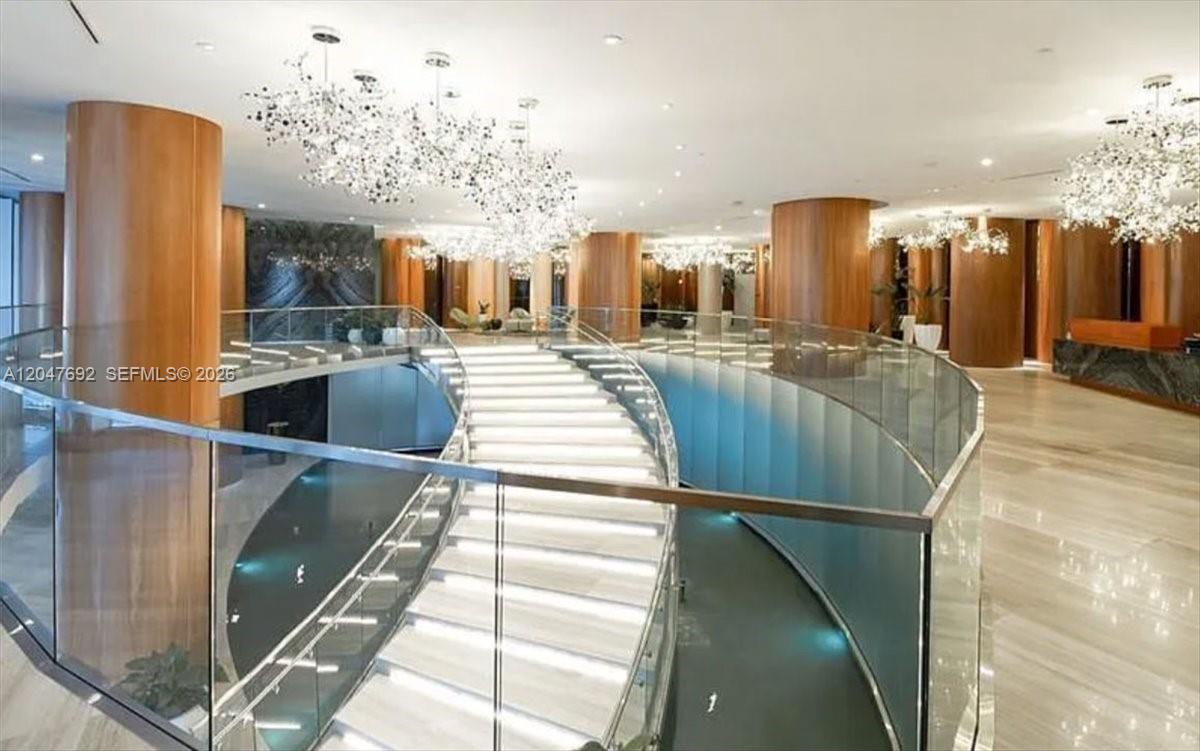 A grand curved staircase with glass railings sits in a lobby with wood columns — 488 NE 18th St # 1806, Miami FL 33132, MIAMI, FL