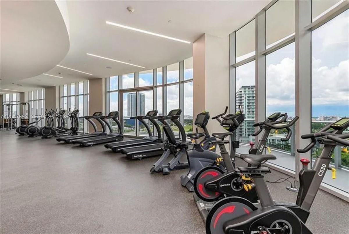 A modern gym features rows of treadmills and stationary bikes next to floor-to-ceiling windows — 488 NE 18th St # 1806, Miami FL 33132, MIAMI, FL