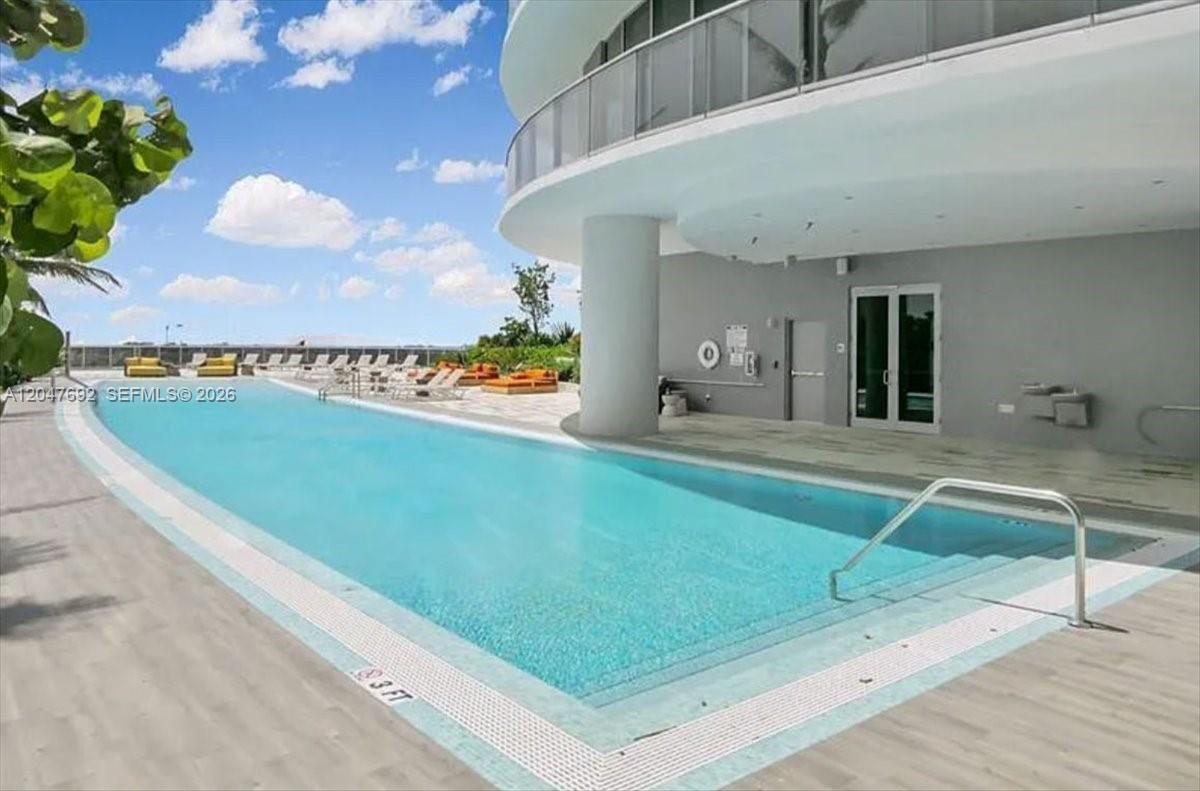 A rectangular swimming pool sits on a patio next to a modern building — 488 NE 18th St # 1806, Miami FL 33132, MIAMI, FL