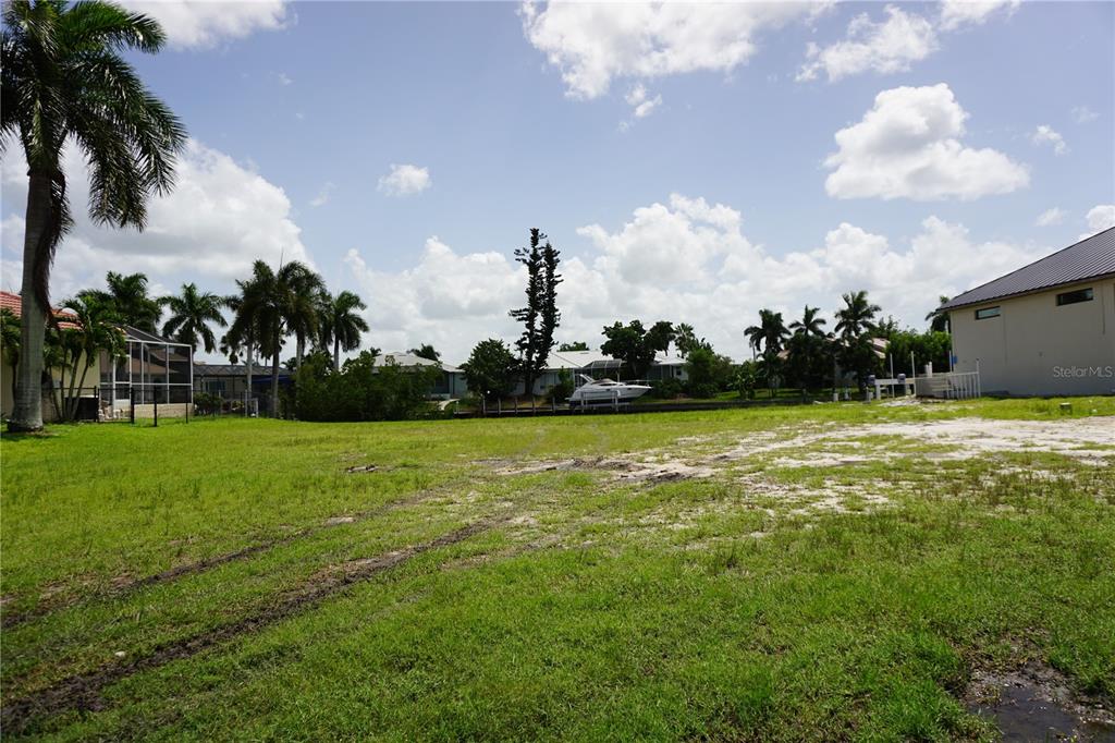 A grassy vacant lot features palm trees and a view of a canal with a boat — 1417 KITTIWAKE DRIVE, PUNTA GORDA, FL