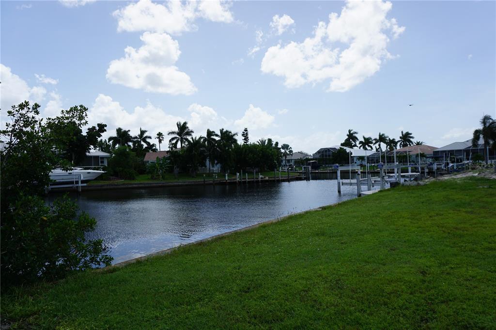 A grassy lawn overlooks a canal with boat docks and palm trees under a cloudy sky — 1417 KITTIWAKE DRIVE, PUNTA GORDA, FL