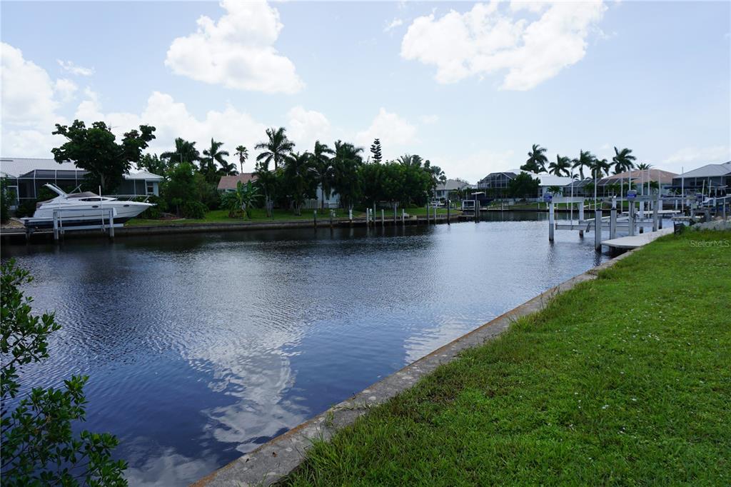 A canal view features a grassy bank, a boat lift, and palm trees under a sky — 1417 KITTIWAKE DRIVE, PUNTA GORDA, FL