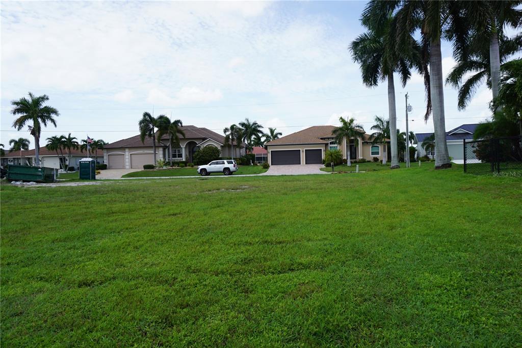 A grassy vacant lot sits in front of two suburban houses with palm trees — 1417 KITTIWAKE DRIVE, PUNTA GORDA, FL