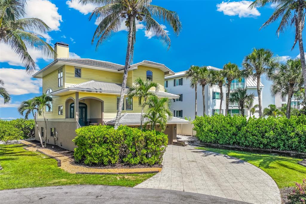 A yellow two-story house with a paved driveway and palm trees under a blue sky — 16776 GRANDE QUAY DRIVE, BOCA GRANDE, FL