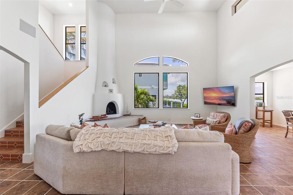 A living room features a high ceiling, a curved fireplace, and large windows overlooking water — 16776 GRANDE QUAY DRIVE, BOCA GRANDE, FL