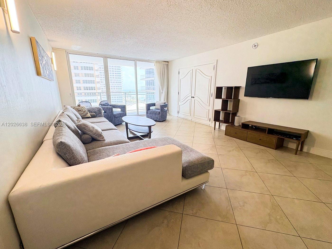 A living room features a large sectional sofa, a wall-mounted television, and floor-to-ceiling windows — 2030 S Ocean Dr # 723, Hallandale Beach FL 33009, HALLANDALE BEACH, FL