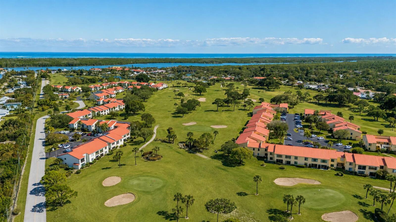 An aerial view of a golf course community with multi-story buildings and a distant ocean — 5403 SE Miles Grant Road # 209, Stuart FL 34997, STUART, FL