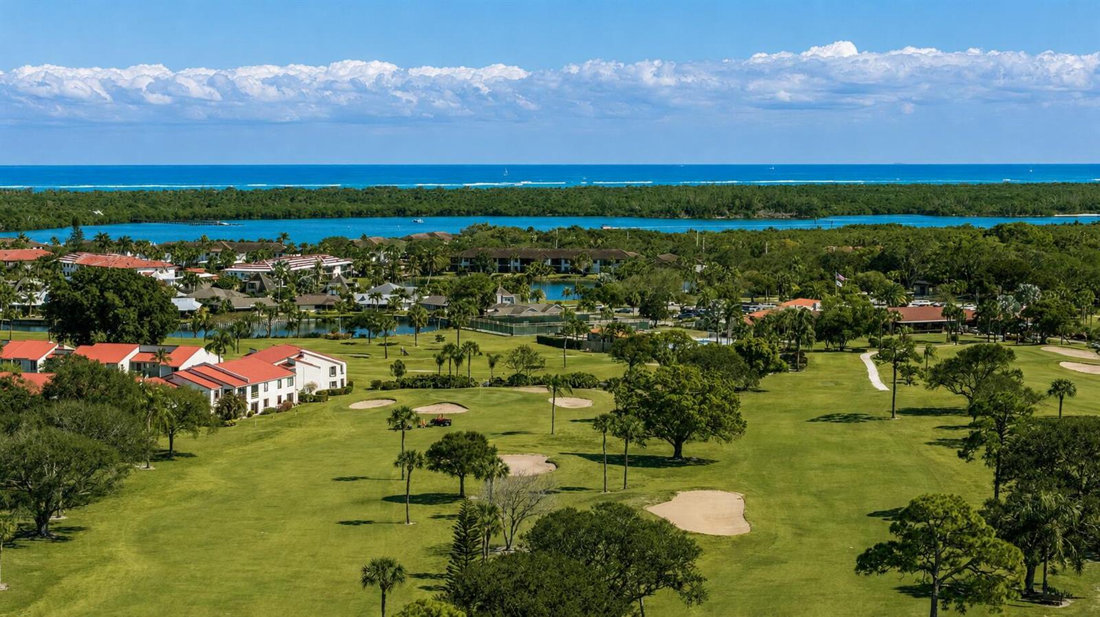 An aerial view of a golf course with residential buildings, lush trees, and the ocean beyond — 5403 SE Miles Grant Road # 209, Stuart FL 34997, STUART, FL